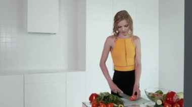 Sebze salatası için domates doğrayan genç bir kadın. Beyaz modern mutfak. Sebze, domates, kırmızı biber, marul, salatalık, avokado. 4k