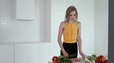 Sebze salatası için domates doğrayan genç bir kadın. Beyaz modern mutfak. Sebze, domates, kırmızı biber, marul, salatalık, avokado. 4k