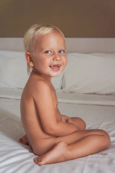 The child sits on the bed and laughs. the child smiles. side view. body