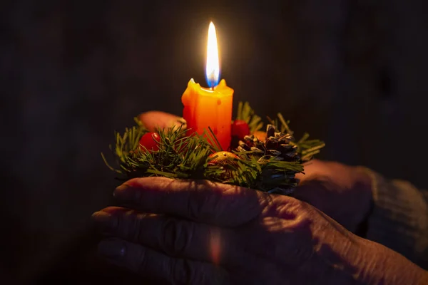 Händerna på en äldre kvinna som håller i ett julljus. — Stockfoto