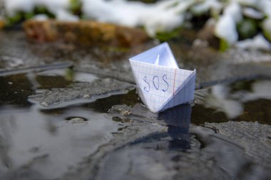 A paper boat with the inscription SOS stuck in the ice. clipart
