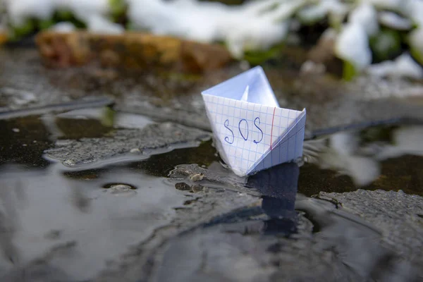 A paper boat with the inscription SOS stuck in the ice. — Stock Photo, Image