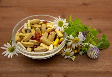 İçinde çeşitli kapsüller, tabletler, tıbbi ve aromatik otlar bulunan bir kase.. 