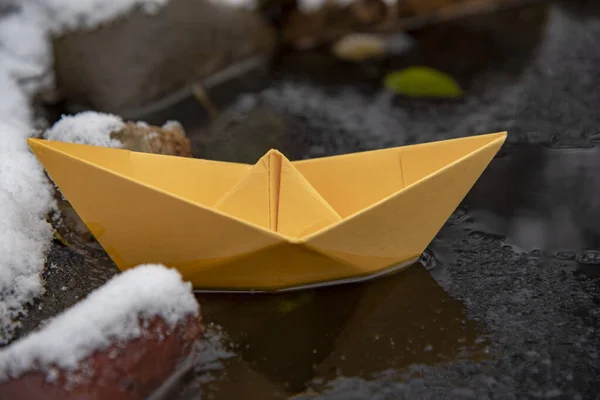 Barca di carta gialla bloccata nel ghiaccio, su una pozzanghera ghiacciata . — Foto Stock