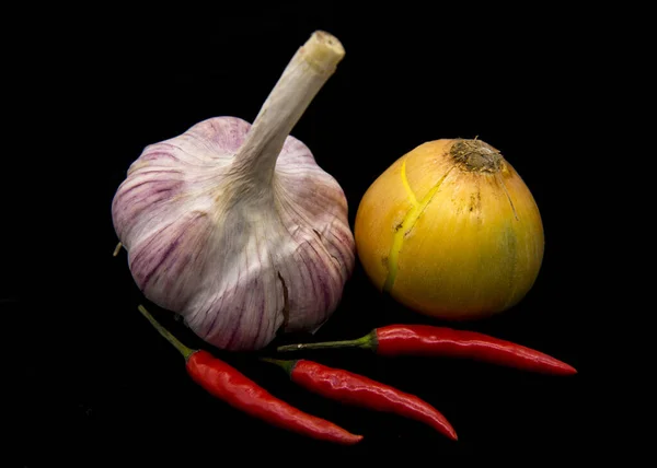 Cebola, alho e vagens de pimenta quente em um fundo preto . — Fotografia de Stock