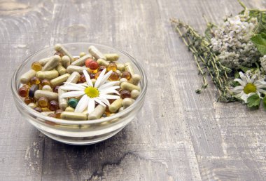 İçinde çeşitli kapsüller, tabletler, tıbbi ve aromatik otlar bulunan bir kase.. 