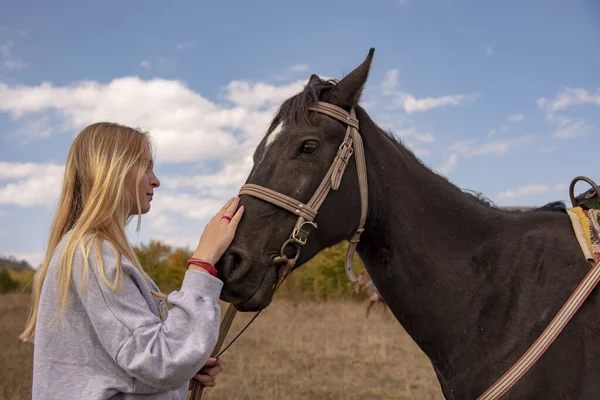 En ung flicka med blont hår smeker försiktigt den bruna hästen — Stockfoto