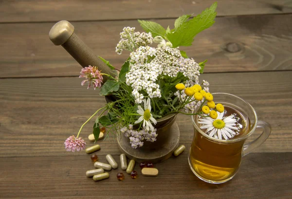 Um morteiro com ervas medicinais, ao lado de uma xícara transparente de chá e cápsulas — Fotografia de Stock