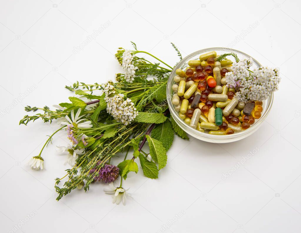 A bowl with various capsules and tablets, medicinal and aromatic herbs. 