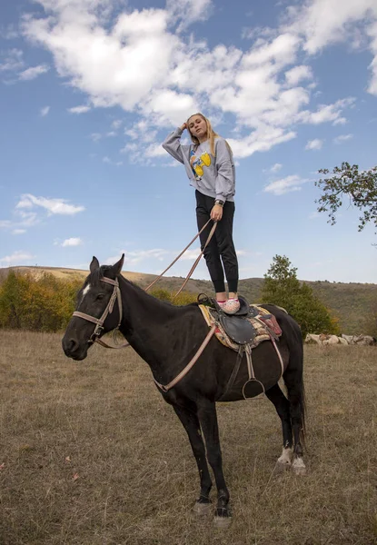 En flicka står på baksidan av en häst mot en bakgrund av en molnig himmel. — Stockfoto