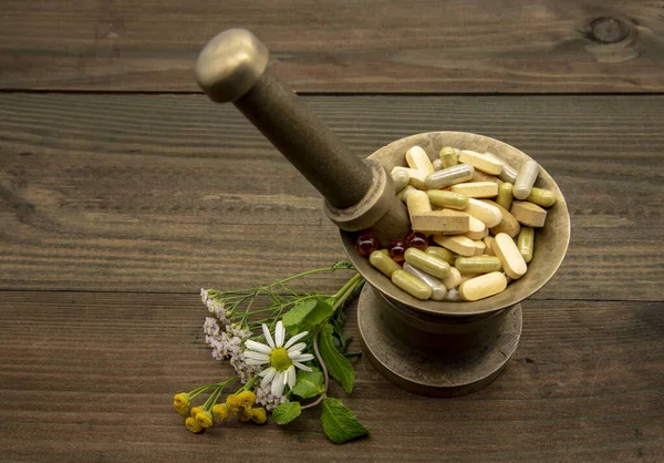 Un mortero de cobre lleno de cápsulas y pastillas. Cerca se encuentran hierbas medicinales . — Foto de Stock