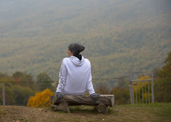 A menina se senta em um banco na encosta Campos e montanhas esticadas diante dela . — Fotografia de Stock