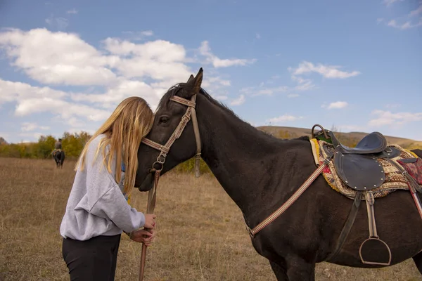En tonårsblond flicka håller i hästens betsel. — Stockfoto