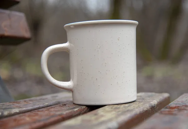 Mug on a wooden bench on a blurred background. — Stock Photo, Image