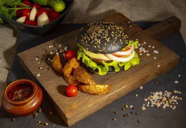 Servis panosunda patates, sebze ve sos ile siyah hamburger..