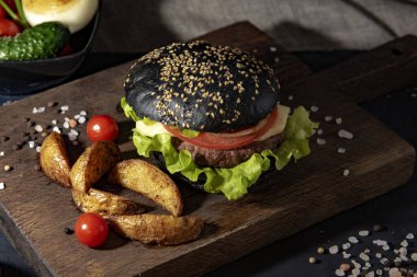 Servis panosunda patates, sebze ve sos ile siyah hamburger..