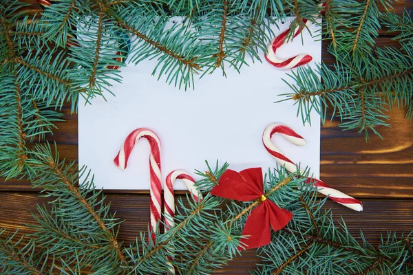 Sobre un fondo de madera hoja de papel blanco rodeado de ramas de abeto azul y dulces de Navidad . — Foto de Stock