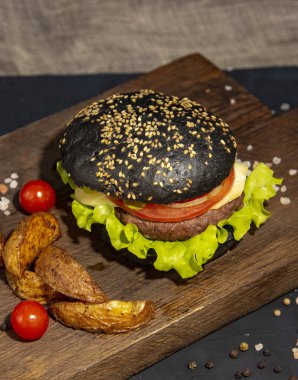 Servis panosunda patates, sebze ve sos ile siyah hamburger..