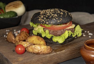 Servis panosunda patates, sebze ve sos ile siyah hamburger..