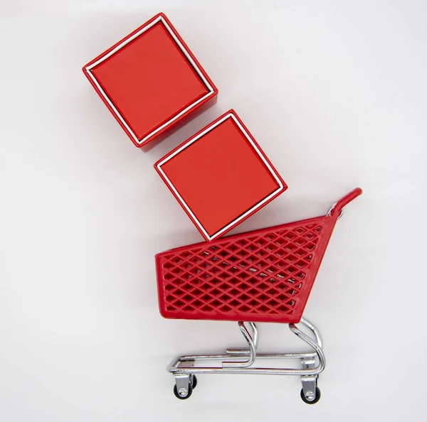 Carrito de compras y cajas de regalo rojas sobre un fondo claro . — Foto de Stock