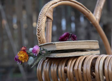 A book and dried flowers lie on a wicker rocking chair clipart