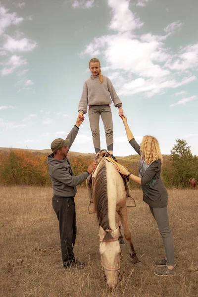 En tonårstjej står på en häst, stödd på båda sidor av vuxna. — Stockfoto