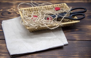 Kraft kağıdının üzerinde makas, kalın iplik ve kırmızı keçeli kalple hasır bir sepet duruyor.