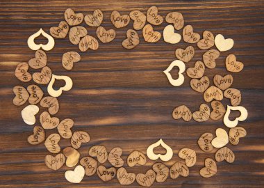 A frame of many wooden hearts on a dark wooden background. 