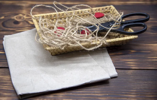 A wicker basket with scissors, coarse thread, and red felt hearts stands on Kraft paper — Stock Photo, Image