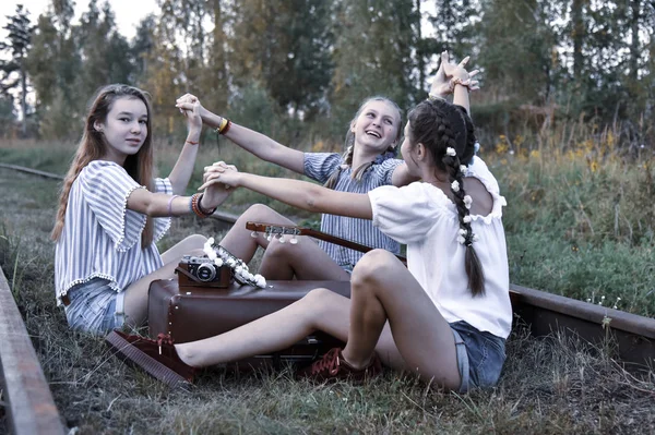 Tres adolescentes se sientan en pistas con una maleta vintage, una cámara y una guitarra . — Foto de Stock