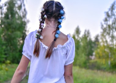 Parlak çiçeklerle örülmüş at kuyruklu bir kız, sırtı kameraya dönük durur.