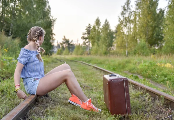 Uma adolescente está sentada com uma mala nos trilhos ferroviários . — Fotografia de Stock
