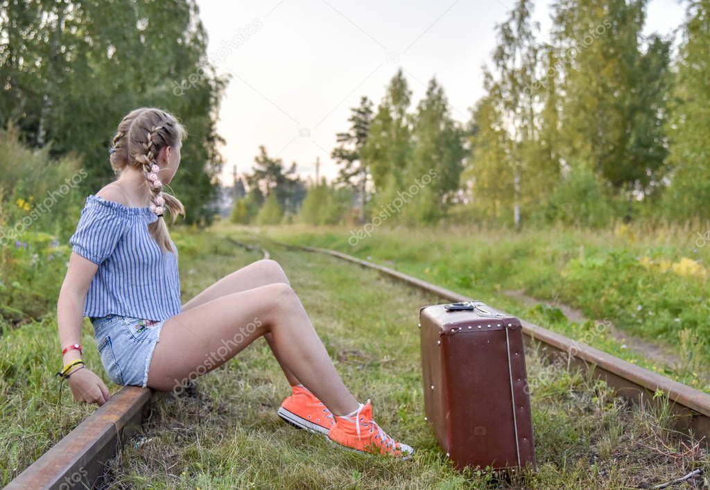 A teenage girl is sitting with a suitcase on the railway tracks.