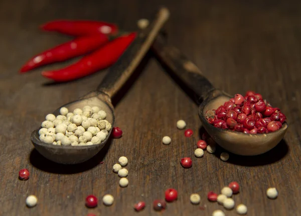 Dos cucharas de madera con pimienta roja y blanca sobre una superficie de madera . —  Fotos de Stock