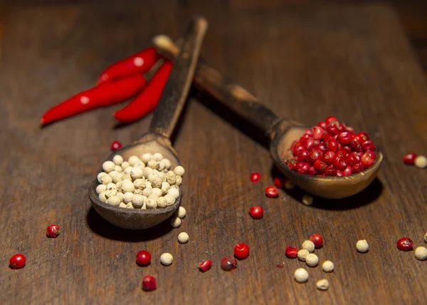 Two wooden spoons with red and white pepper on a wooden surface. — ストック写真