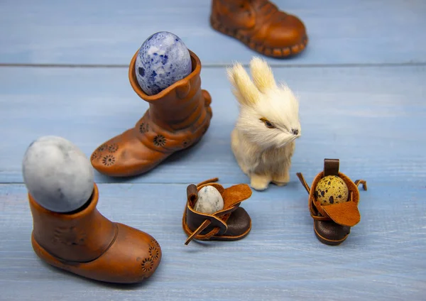 Кролик и различные сапоги с пасхальными яйцами на голубой деревянной поверхности — стоковое фото