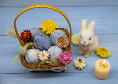 Bir sepet dolusu Paskalya yumurtası maviye boyanmış bir tavşan ve yanan mumlar.