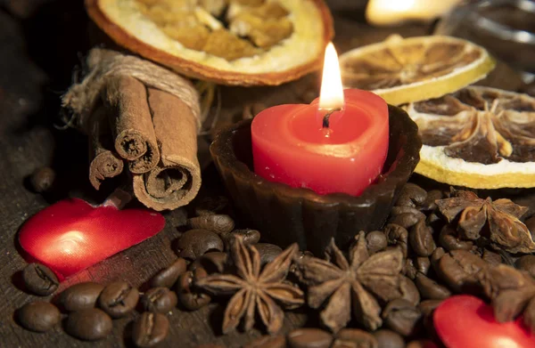 Hořící svíčka, různé druhy koření, sušené pomeranče a malé sněhové pusinky na dřevěné desce stolu. — Stock fotografie