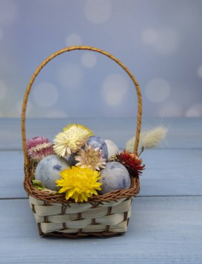 Kurumuş çiçeklerle süslenmiş, ahşap bir arka planda renkli Paskalya yumurtalarıyla dolu bir sepet..