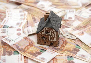 Seramik bir ev, arka planda beş bin ruble banknot yığını üzerinde duruyor. Başarı sembolü, sermaye birikimi, yaşam koşullarının iyileştirilmesi