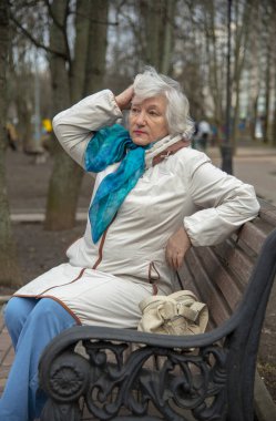 Zarif, yaşlı, gri saçlı bir kadın baharın başında bir bankta oturuyor..