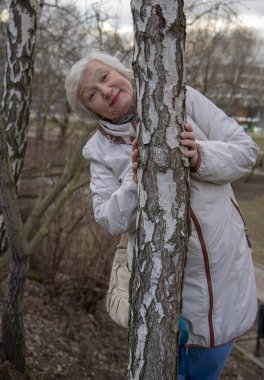 Ağaçların yanında güzel, kır saçlı, yaşlı bir kadın. Sağlıklı yaşam süresi.