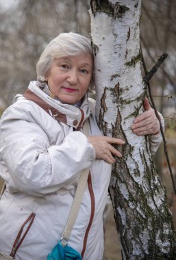 Ağaçların yanında güzel, kır saçlı, yaşlı bir kadın. Sağlıklı yaşam süresi.