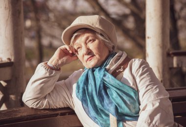 Zarif, yaşlı, gri saçlı bir kadın baharın başında bir bankta oturuyor..