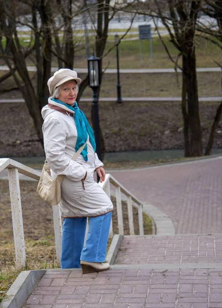 カメラに面した公園の階段にはフリットベレー帽をかぶった年配の女性が立っていた — ストック写真