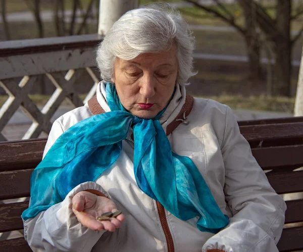 A sad old woman is sitting on a Park bench with an empty purse and change in her hand.
