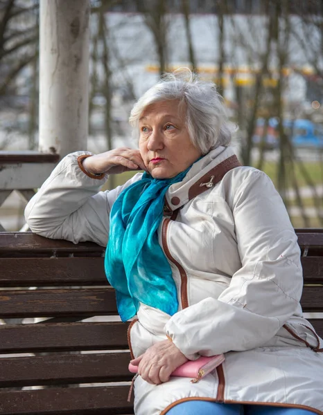 一位悲伤的老妇人正坐在公园的长椅上 手里拿着一个粉色的钱包 — 图库照片