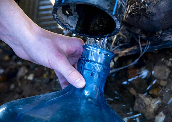 Heren handen vullen een plastic fles met water uit een veer. — Stockfoto