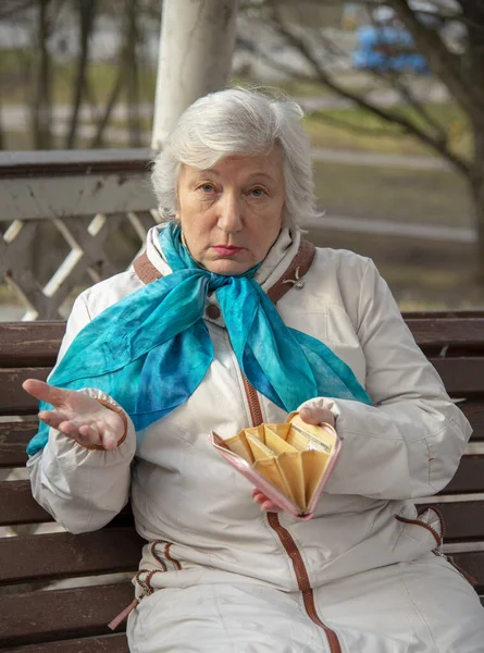 Eine traurige, elegant gekleidete, ältere Frau sitzt mit leerem Geldbeutel in der Hand auf einer Parkbank. — Stockfoto
