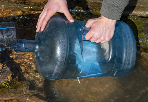 Heren handen vullen een plastic fles met water uit een veer. — Stockfoto